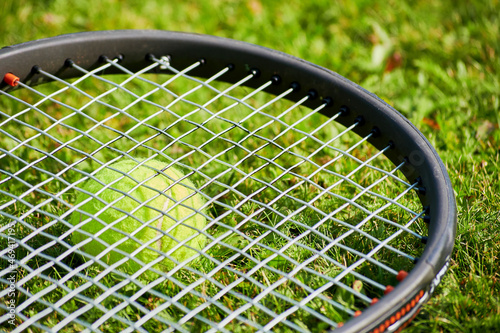 Tennis racket and a yellow ball on the grass court. Individual sports and outdoor games