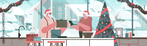 senior couple in santa hats cooking together in kitchen christmas dinner preparation new year holidays celebration