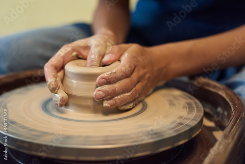 Hands of young craftsperson holding by rotating pottery wheel while working over new artisan clay items in workshop