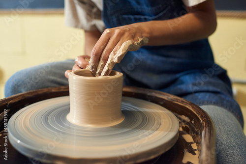Hands of young female potter sitting by rotating pottery wheel while working over new collection of earthenware