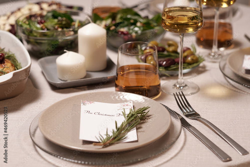 Part of served festive table with postcard on plate, candles on square porcelain tray, glasses with wine and food in bowls Part of served festive table with postcard on plate, candles on square porcelain tray, glasses with wine and food in bowls