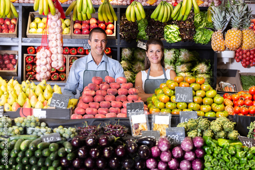 Glad male and female shop assistants in vegetable shop