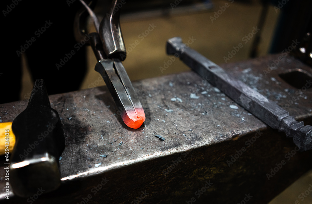 A glowing piece of metal on an anvil held by a pair of metal tongs