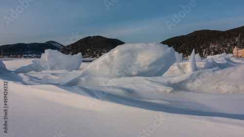 On a frozen lake, icy snow forms bizarre figures. In the distance, against the background of the blue sky, a wooded mountain range is visible. Baikal