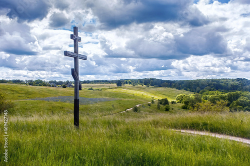 The wooden orthodox cross with the green fields on the background