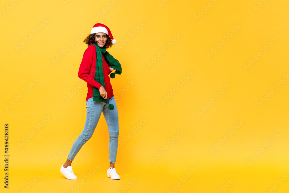 Fototapeta premium Full length portrait of fun happy Afircan American woman in Christmas attire dancing on isolated yellow studio background with copy space