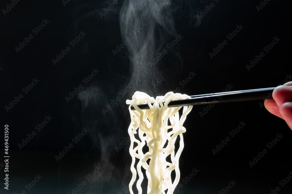 Lift with wood chopsticks to pickup noodle with steam and smoke on black background. korea, japan, china, Vietnam and Asian noodle junk food concept Lift with wood chopsticks to pickup noodle with steam and smoke on black background. korea, japan, china, Vietnam and Asian noodle junk food concept