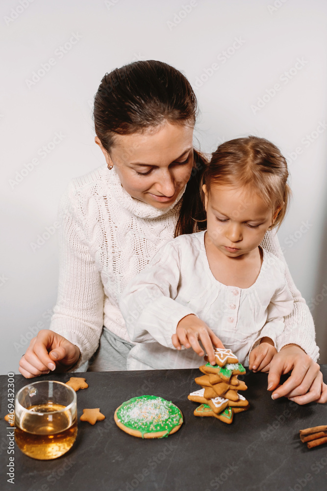 Mother with child decorating gingerbread cookies with icing for Christmas. Homemade festive food. Cute toddler girl Family Workshop. Stars, tree