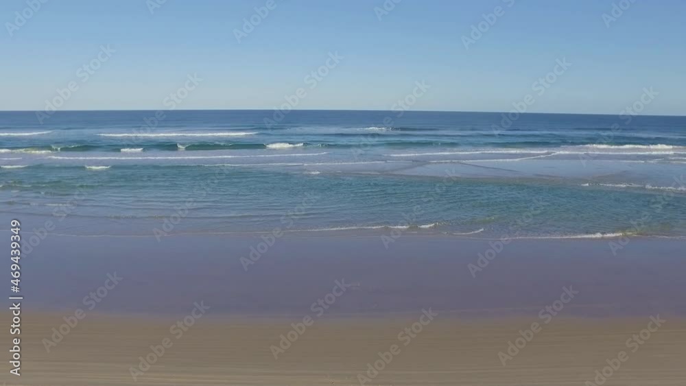 Slow and smooth aerial drone shot flying out over the clear azure waters off the beach of Fraser Island and out over the surf under clear blue skies Slow and smooth aerial drone shot flying out over the clear azure waters off the beach of Fraser Island and out over the surf under clear blue skies