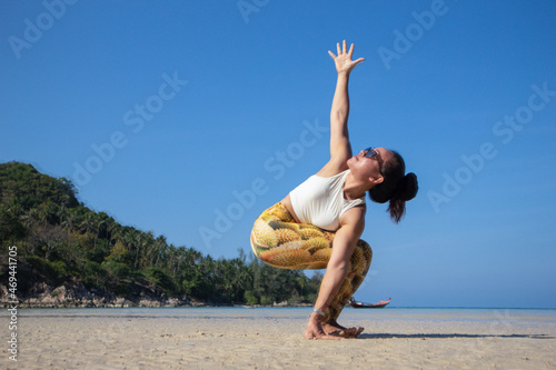 Revolved Chair with Arms Extended. Asian woman doing yoga poses on a beach in Koh Pha Ngan island, Thailand