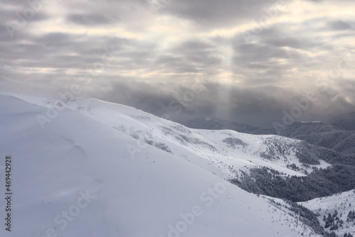 Snow-covered mountain slopes against the backdrop of a cloudy sky. Snow-covered mountain slopes at sunset.