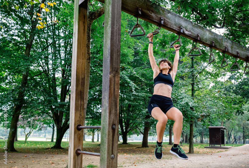 Female athlete doing monkey exercises on rings in a park