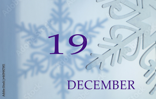 Calendar for December 19: name of the month in English, number 19 on a blue background of snowflakes and their shadows.