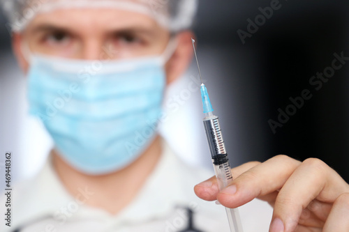Doctor with syringe in hand  man in medical mask preparing to injection. Concept of vaccination during covid-19 pandemic