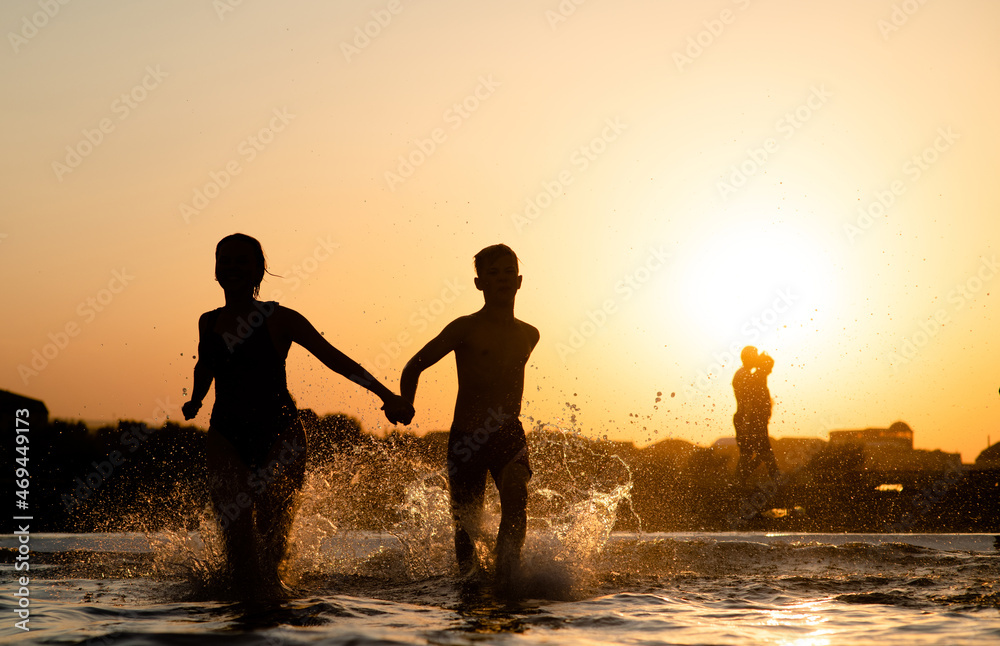 Happy kids running and splashing in the sea at sunset. Summer vacation and healthy lifestyle concept. Empty space for text