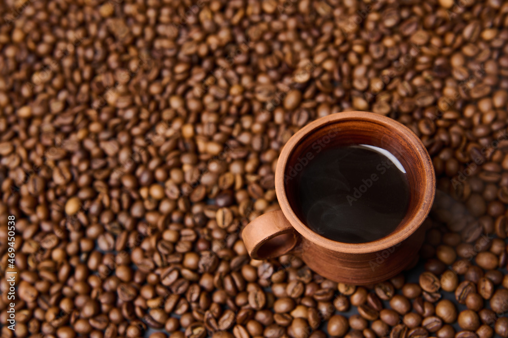 Close-up composition of a clay coffee cup with freshly brewed coffee drink with steam on the background of freshly roasted coffee beans with copy space for ad. Flat lay, high angle view, still life Close-up composition of a clay coffee cup with freshly brewed coffee drink with steam on the background of freshly roasted coffee beans with copy space for ad. Flat lay, high angle view, still life
