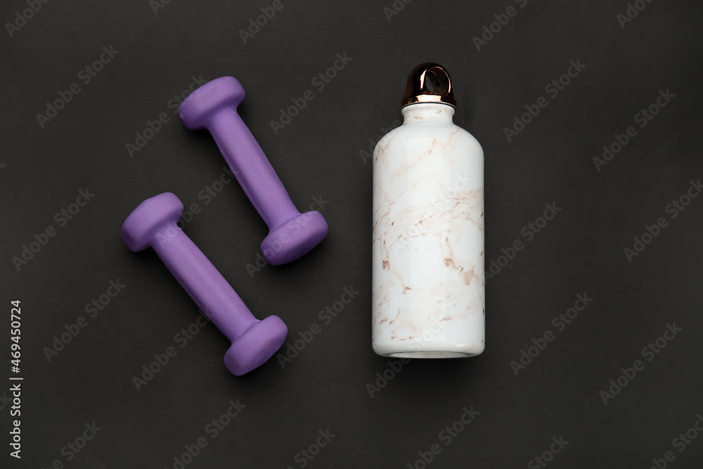 Naklejka premium Dumbbells and bottle of water on dark background