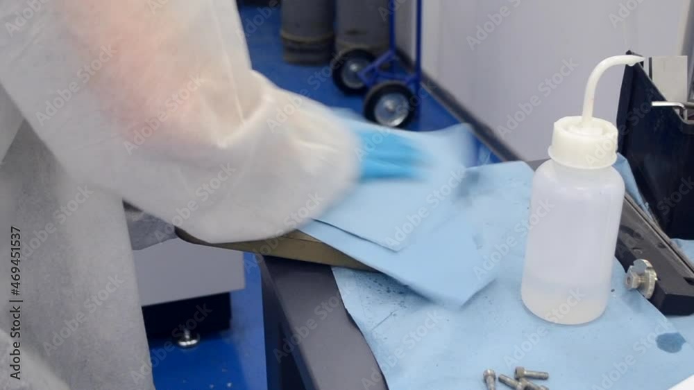 Worker in White Protective Suit and Blue Protective Gloves Cleaning Metal Part Worker in White Protective Suit and Blue Protective Gloves Cleaning Metal Part