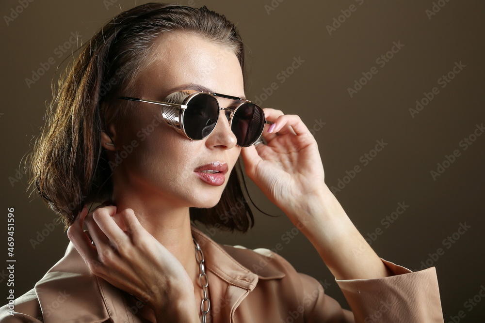 Fototapeta premium gorgeous glamour woman face with professional makeup on dark background. beautiful female face close up on brown background studio shot. fashion model face wearing dark sunglasses