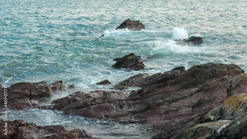 Small waves breaking over rugged rocks on the south Devon coast UK