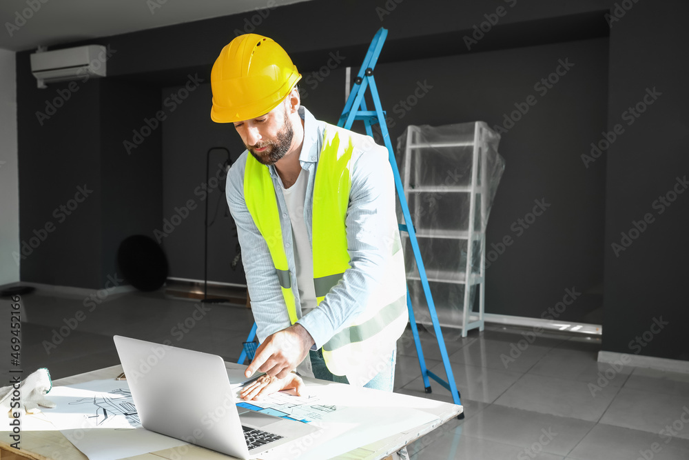Male builder working with laptop at table in room Male builder working with laptop at table in room