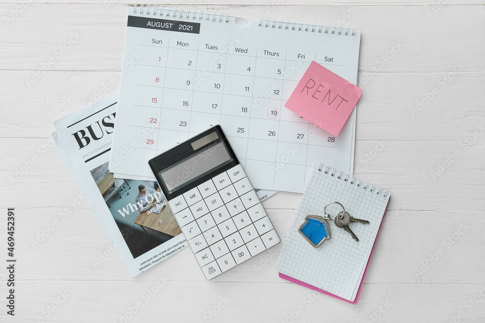 Calendar with pay rent mark, calculator, notepad, newspaper and keys with house shaped keychain on white wooden background Calendar with pay rent mark, calculator, notepad, newspaper and keys with house shaped keychain on white wooden background
