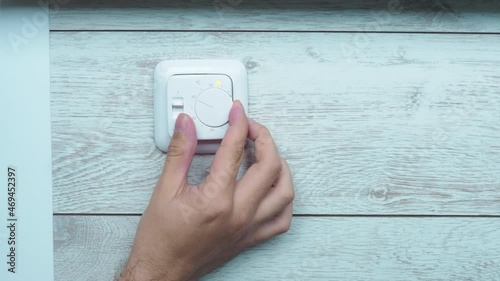 A man's hand turns the wheel of a white plastic floor heating temperature controller