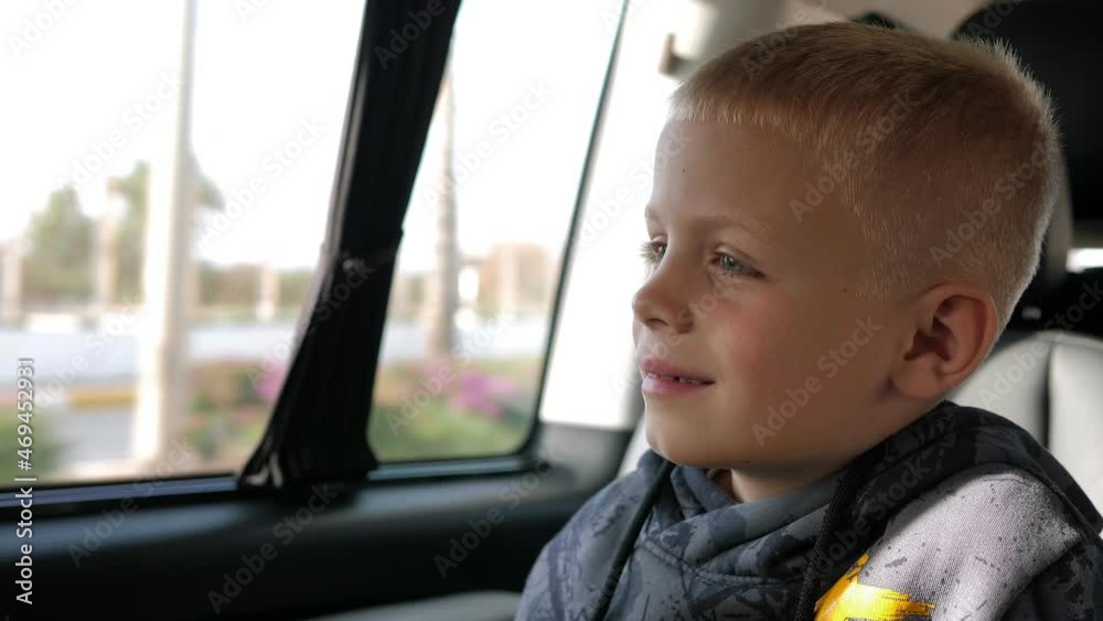 Close-up of a little boy of eight years old riding in a car and looking out the window in summer. Family trip. Close-up of a little boy of eight years old riding in a car and looking out the window in summer. Family trip.