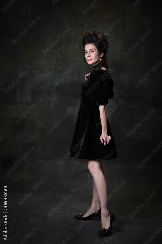 Classic retro portrait of young beautiful woman in image of medieval royal person in black dress isolated on dark vintage background.