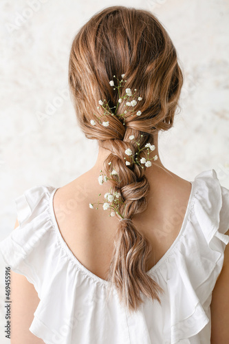 Pretty young woman with flowers in hair on light background