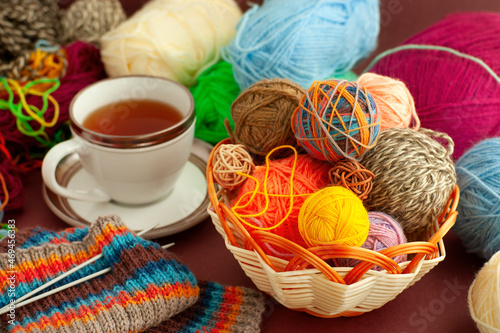 Knitting and tea in a cozy atmosphere. Colorful yarn for knitting in a basket. Cup of tea and knitted scarf close-up.