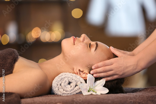 Relaxed young African-American woman getting facial massage by therapist in spa salon