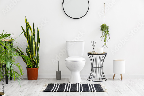 Toilet bowl, houseplants and table with bathroom accessories near white wall