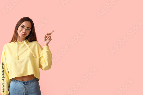 Beautiful young woman in stylish hoodie pointing at something on color background
