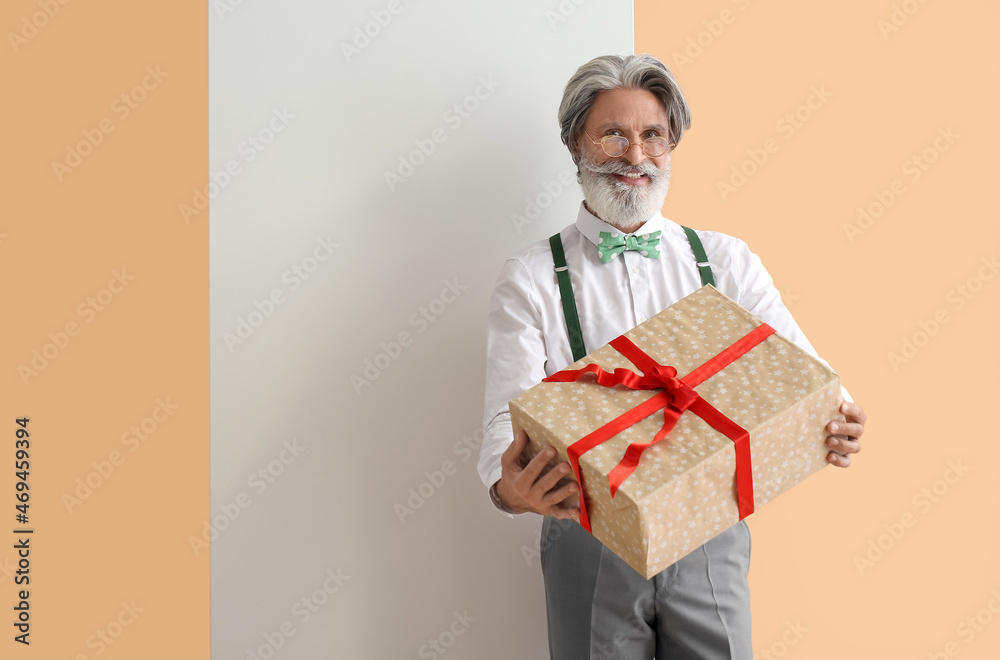 Stylish mature man with blank poster and gift on color background Stylish mature man with blank poster and gift on color background
