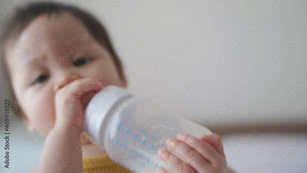 asian baby toddler infant playing on bed walking around then drinking mother food milk from bottle. baby skill development holding milk bottle. asian baby toddler infant playing on bed walking around then drinking mother food milk from bottle. baby skill development holding milk bottle.