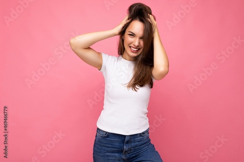 Photo portrait of young beautiful smiling hipster brunette woman in white t-shirt with mockup. Sexy carefree female person posing isolated near pink wall with empty space in studio. Positive model