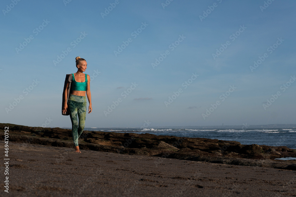 beautiful girl walking on the beach with yoga mat.