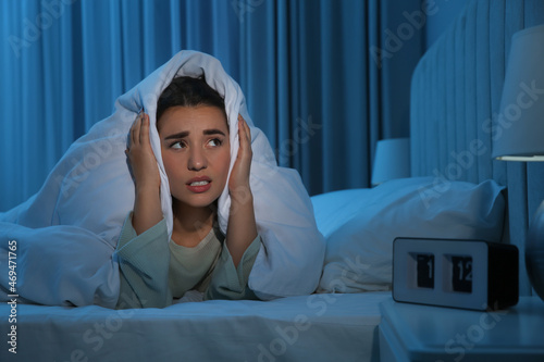Unhappy young woman covering ears with blanket in bed at home. Noisy neighbours photo