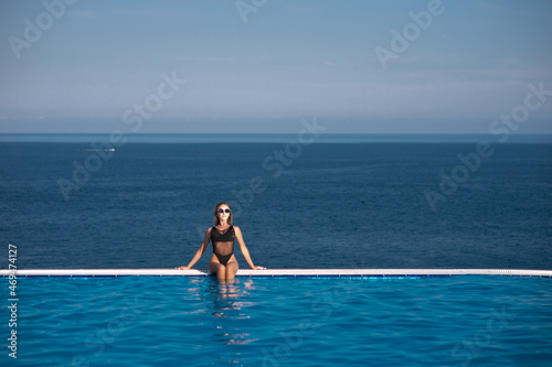 Young woman relaxing in infinity swimming pool looking at view