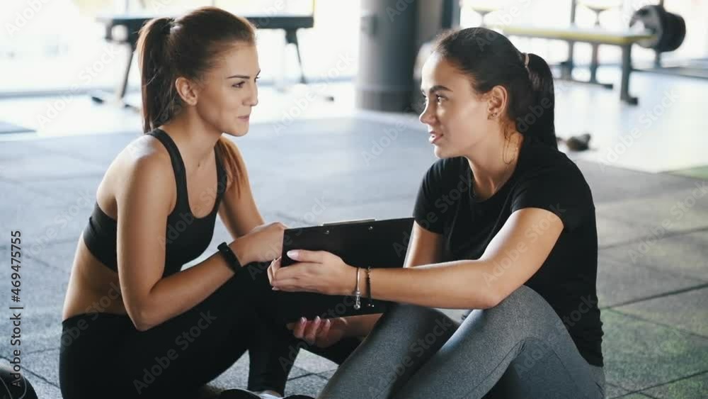 Female personal trainer with notepad showing young woman results Female personal trainer with notepad showing young woman results