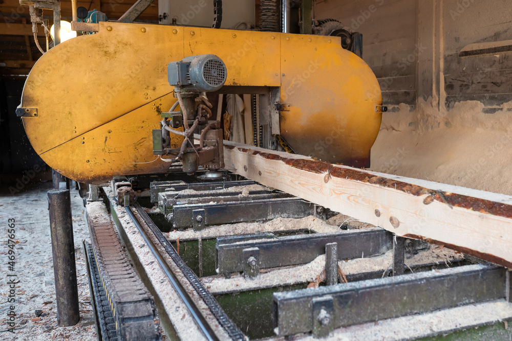 Fototapeta premium Processing wooden boards at a sawmill. The process of processing logs in the equipment of a sawmill saw a tree trunk on boards.