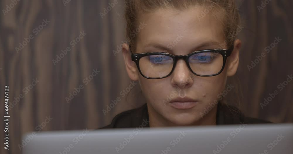 Woman in eyeglasses concentrated, reading and working with laptop, background of wooden wall. Student with device working. Concept of distance learning Woman in eyeglasses concentrated, reading and working with laptop, background of wooden wall. Student with device working. Concept of distance learning