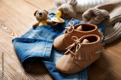 Children's shoes, clothes, toy and pacifier on wooden table