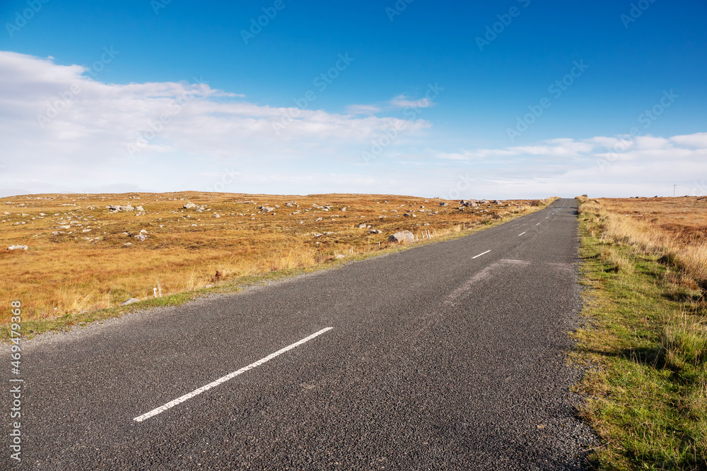 Small narrow asphalt road in a huge empty fields. Clean blue cloudy sky. Warm sunny day. Connemara, Ireland. Travel and transportation concept