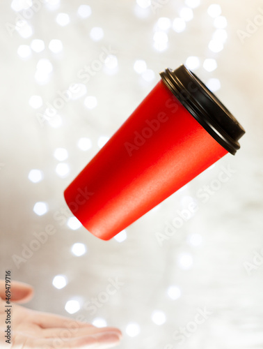 red paper cup for coffee flying in the air against the background of New Year's lighting bokeh