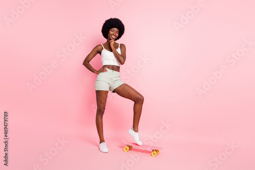 Full body photo of cool young curly hairdo lady ride skate wear white top shorts isolated on pastel pink color background