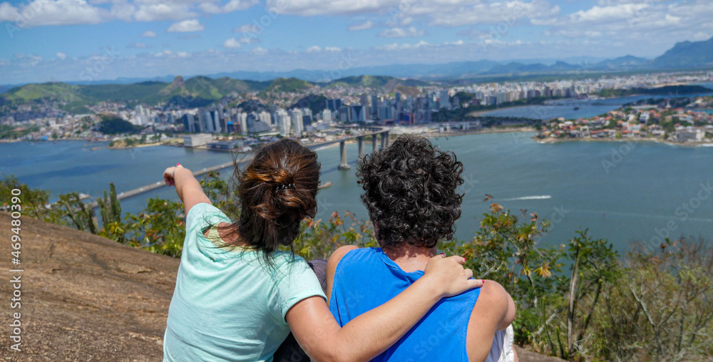 View from Morro do Moreno in Vila Velha city to Vitoria City and the Terceira Ponte Bridge, Vitoria Bay and blue sky. Couple pointing to a subject.