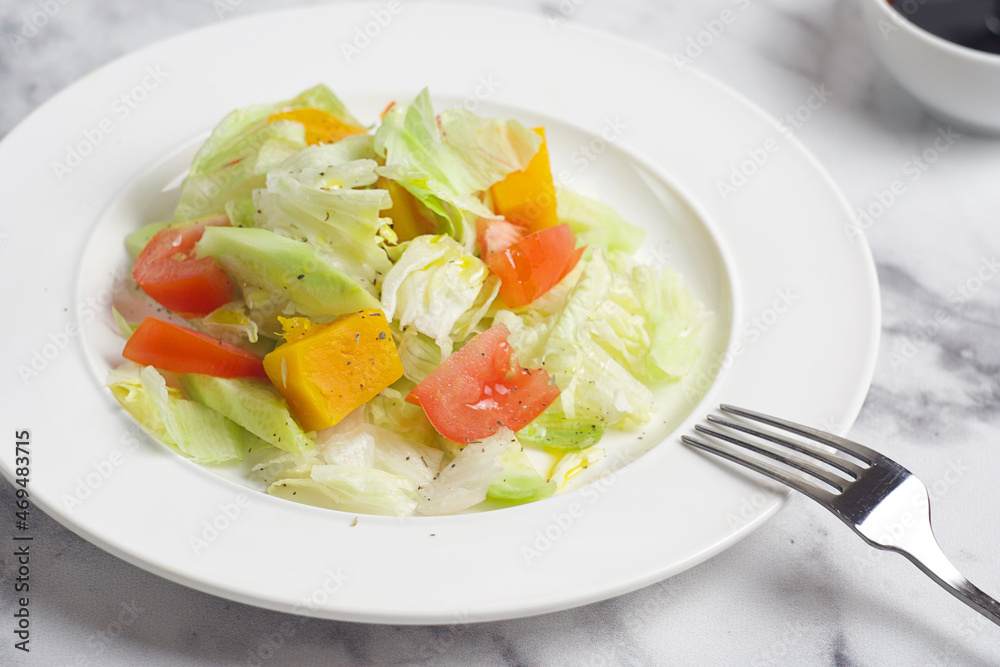 Salad with cabbage, tomatoes, cucumber, pumpkin in a plate on the marble table. Behind there is a gravy boat with sauce. Breakfast Salad with cabbage, tomatoes, cucumber, pumpkin in a plate on the marble table. Behind there is a gravy boat with sauce. Breakfast