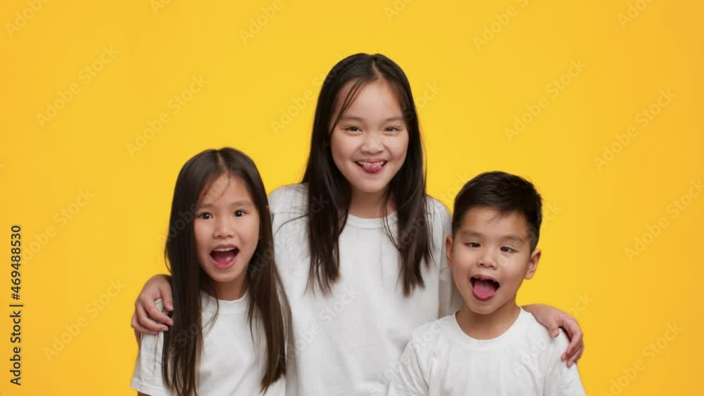Cheerful Japanese Siblings Having Fun Grimacing Showing Tongues, Yellow Background Cheerful Japanese Siblings Having Fun Grimacing Showing Tongues, Yellow Background
